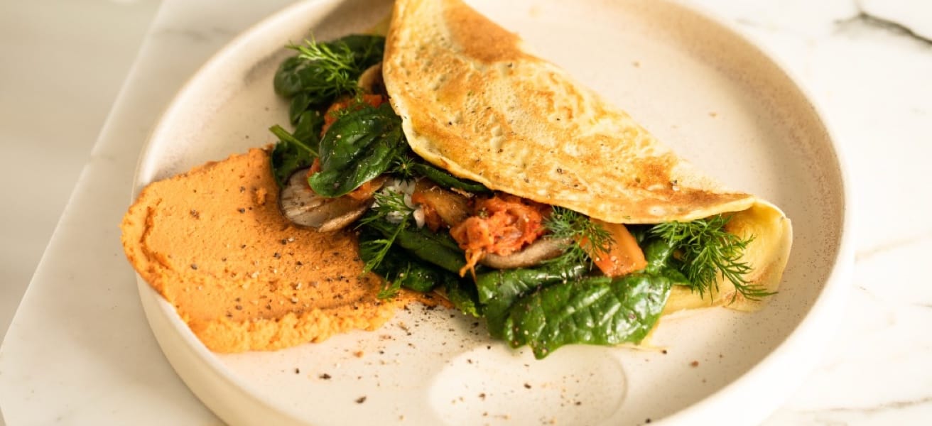 A delicious-looking, restaurant-class omelete inside a white plate, on a white-clothed table 